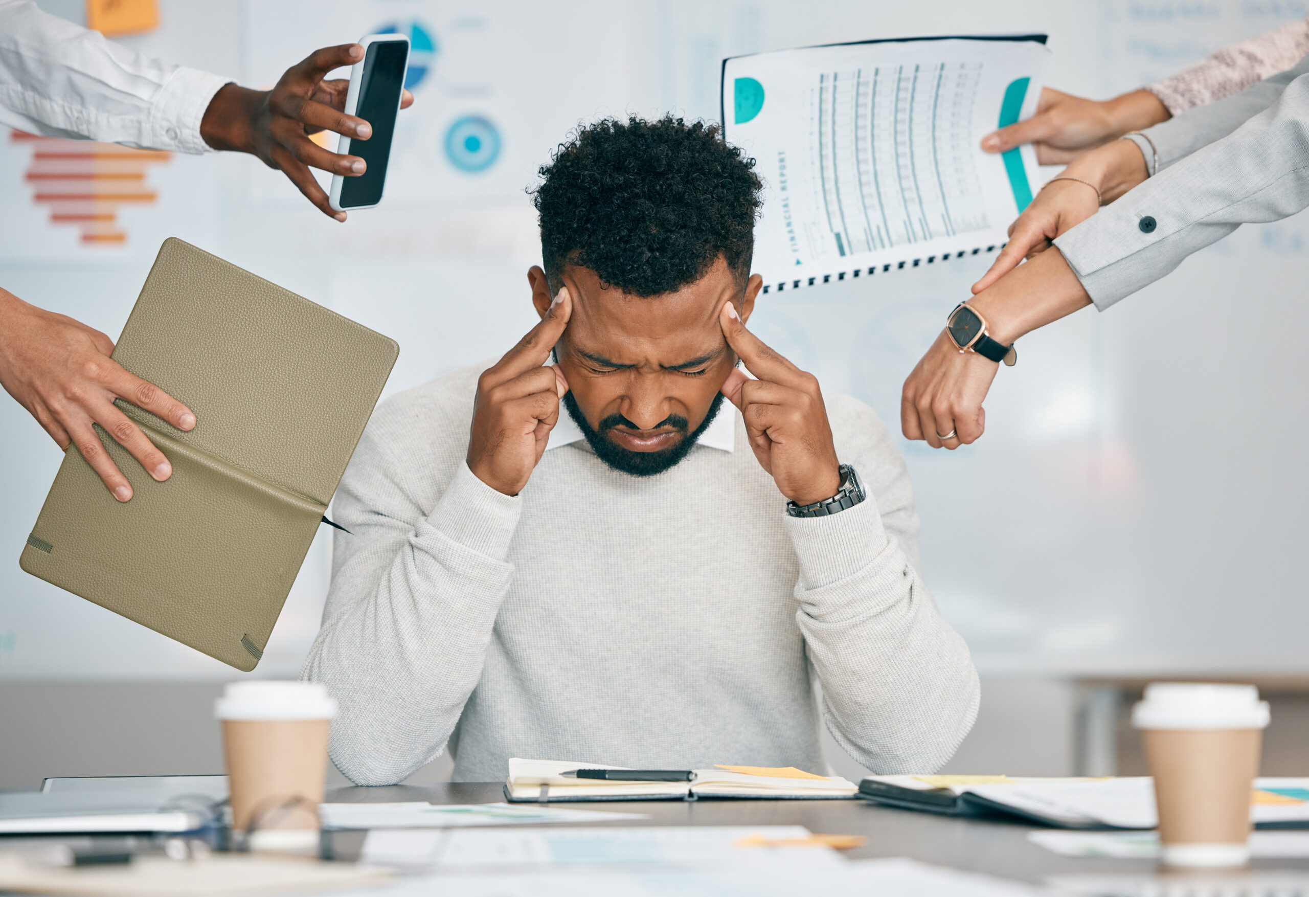 Stress, burnout and tired black man with headache, frustrated or overwhelmed by coworkers at workplace. Overworked, mental health and anxiety of exhausted male worker multitasking at desk in office.